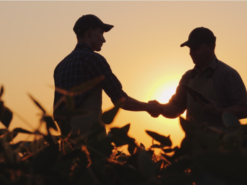2 men in a farm field shaking hands as the sun rises