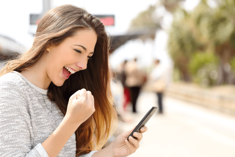 Young woman fist pumping while looking at her smartphone